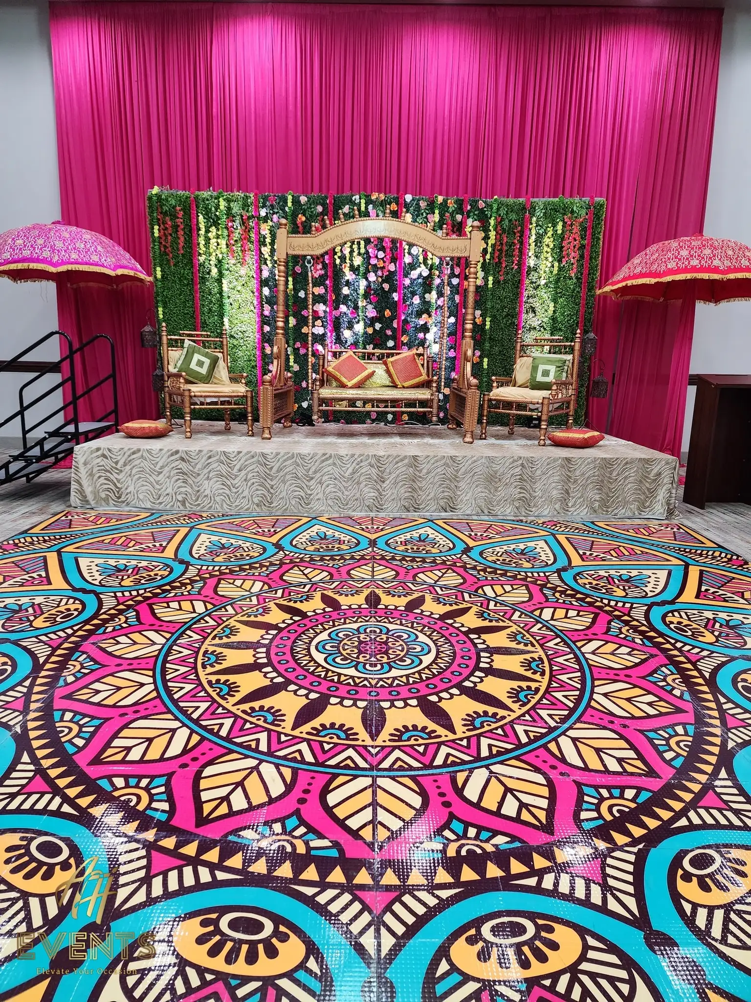 Wooden swing on a stage backed by greenery and magenta drapes, above a mandala floor