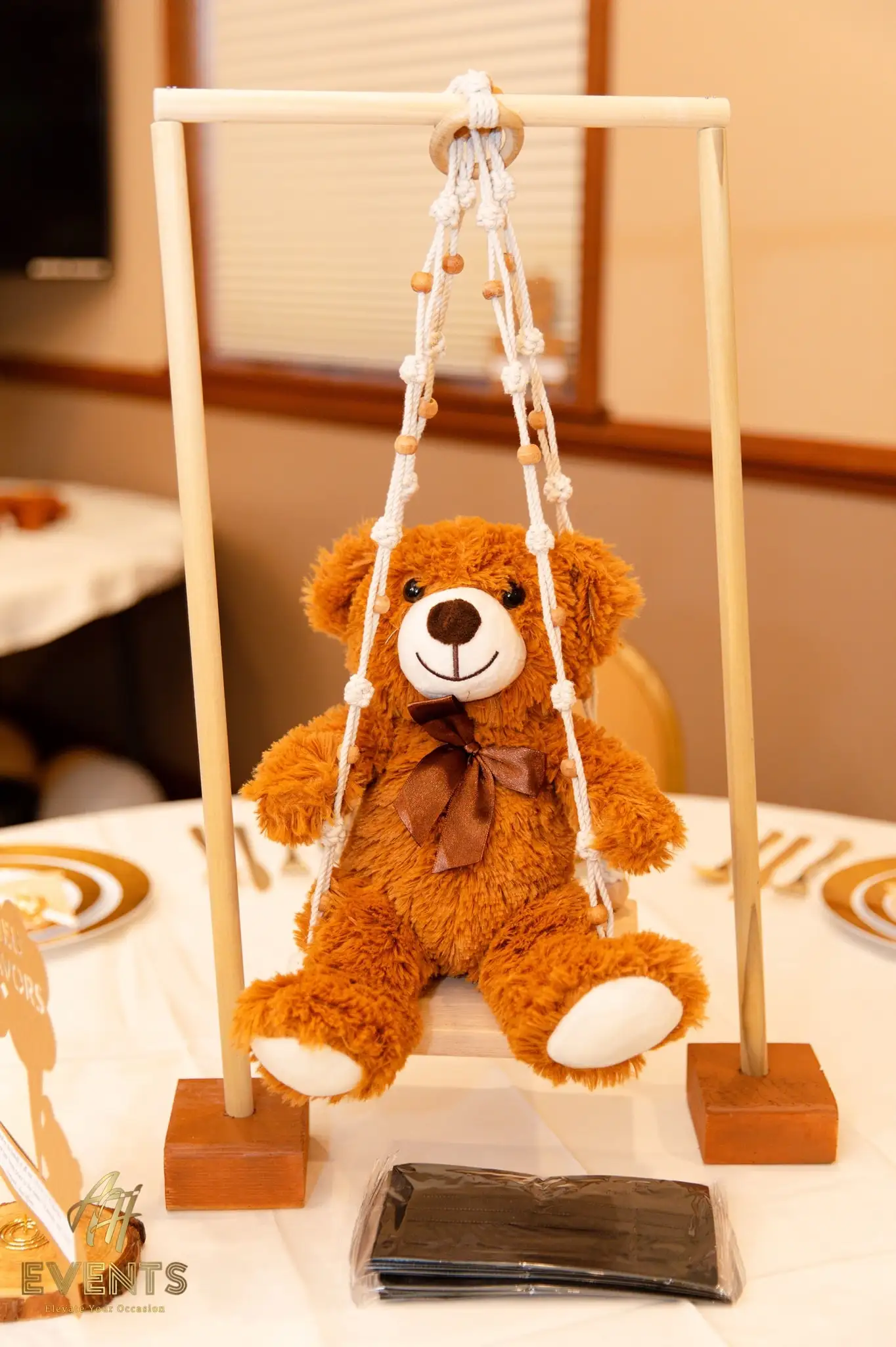 Brown teddy bear on a wooden macramé swing as a table centerpiece