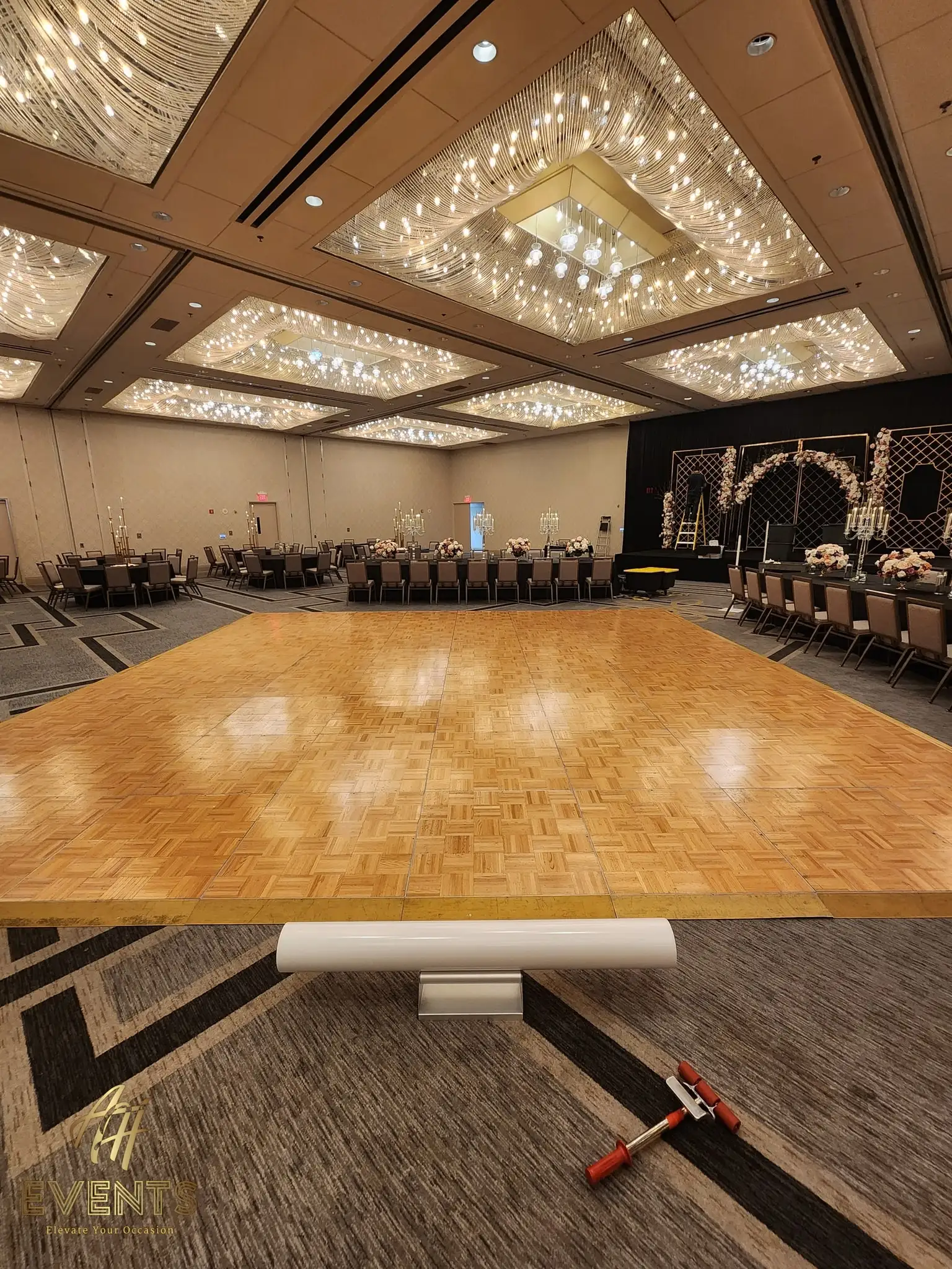 Parquet wood dance floor under a sparkling crystal-strand ceiling, a floral arch stage behind