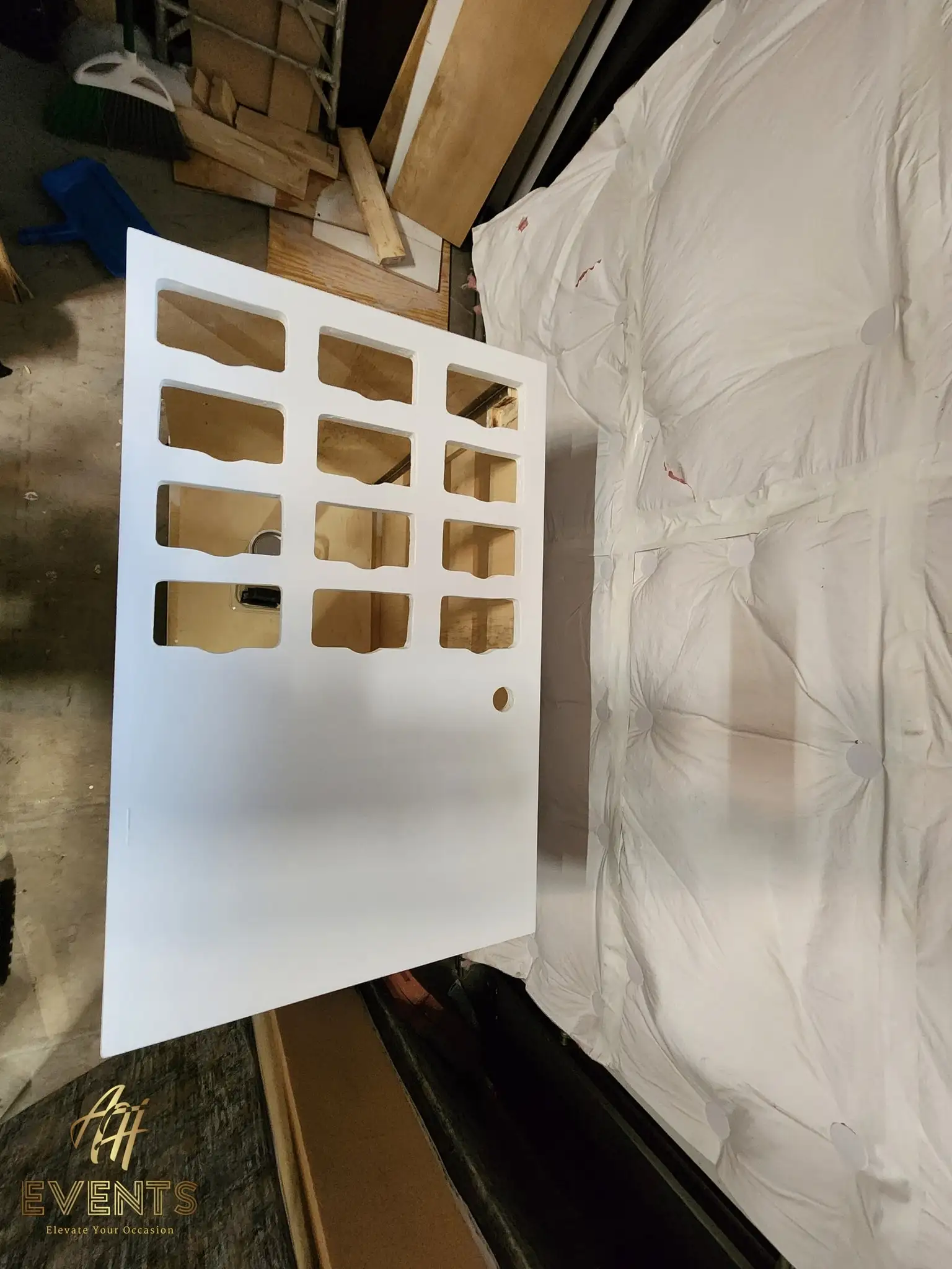 White-painted cart-top panel with a grid of rectangular cup-well cut-outs, propped beside the spray-booth drape