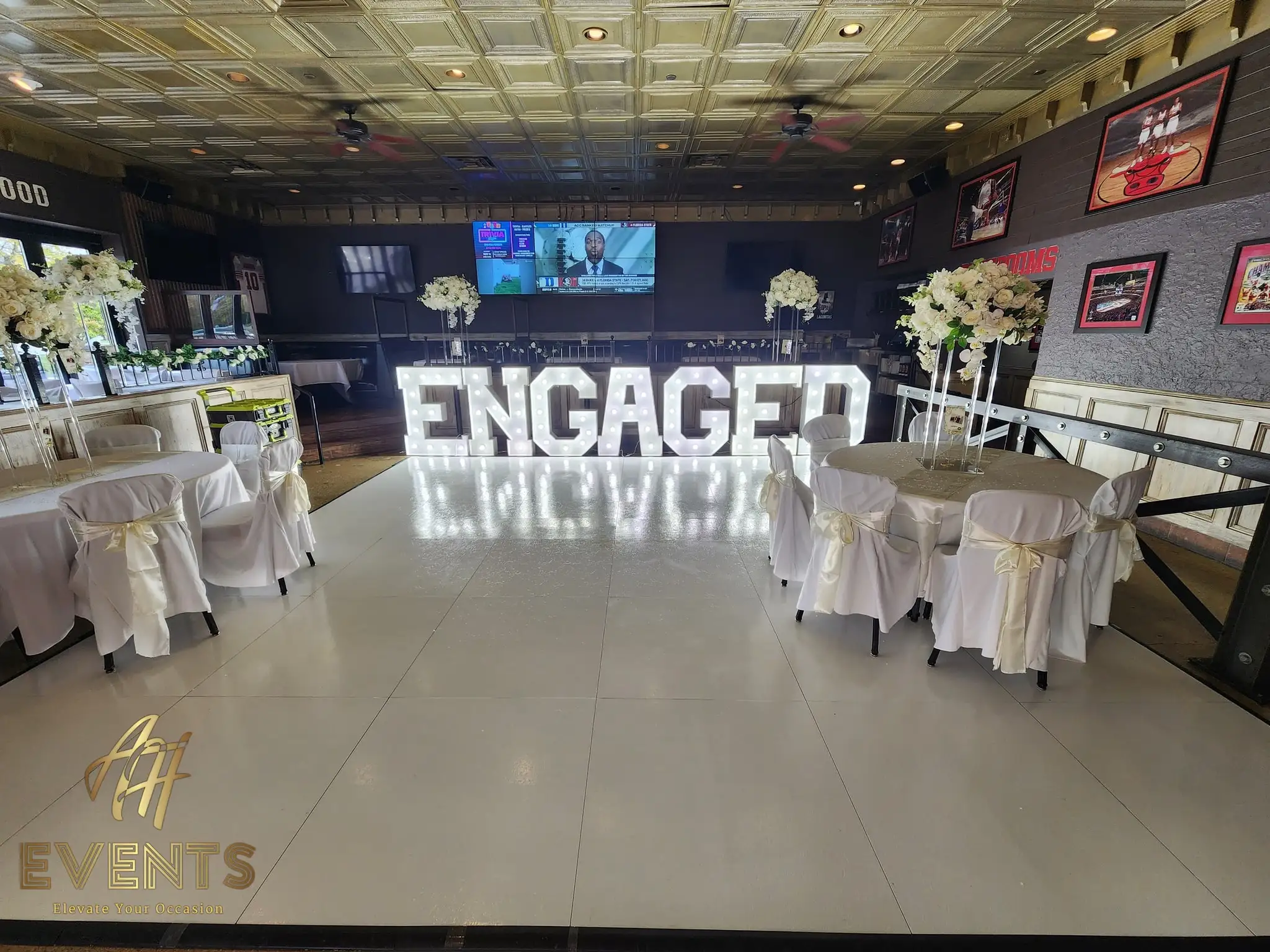 White dance floor in a lounge with light-up 'ENGAGED' marquee letters and white-draped chairs