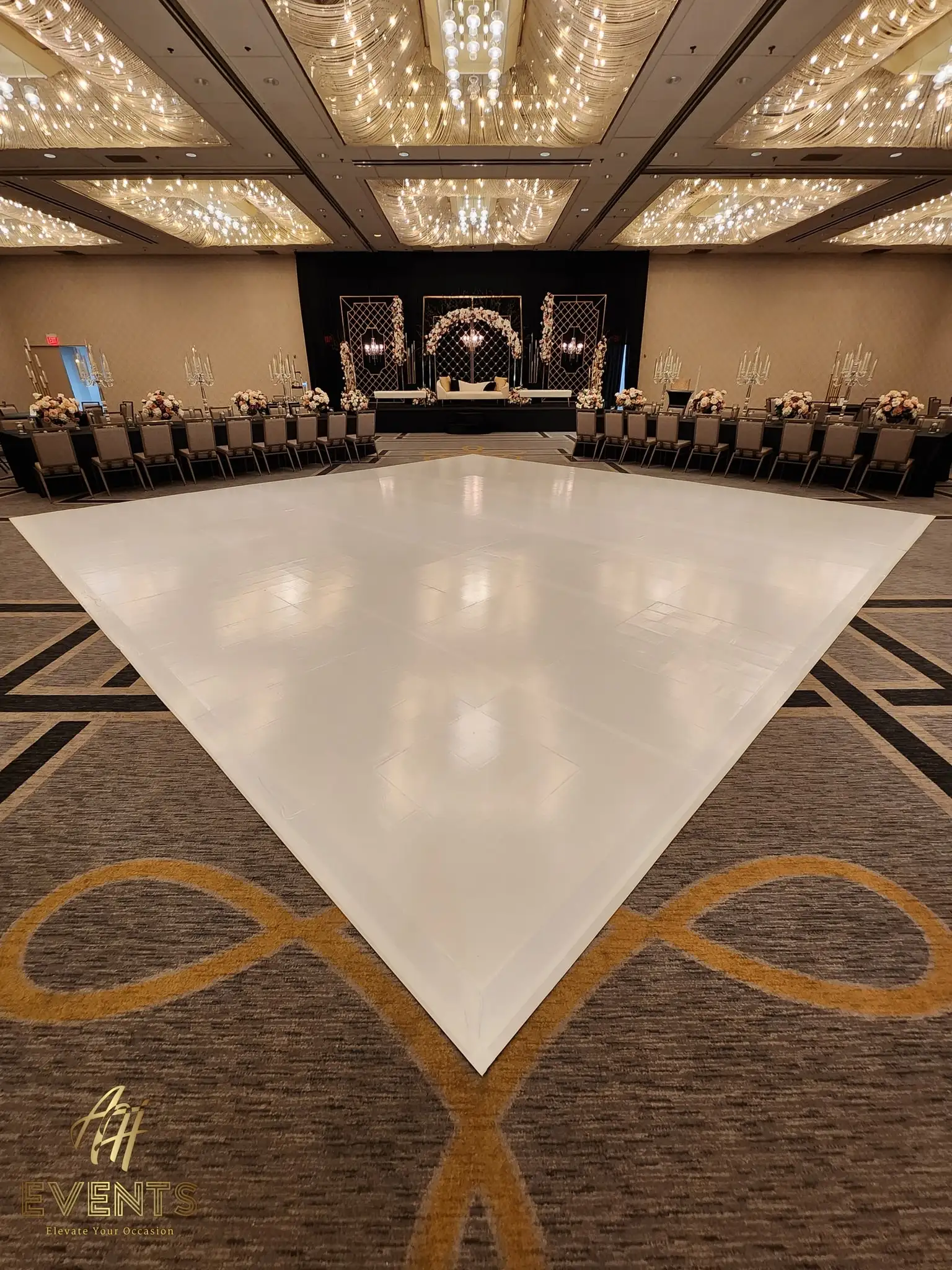 Glossy white dance floor under a crystal-strand ceiling, facing a black stage with a floral arch