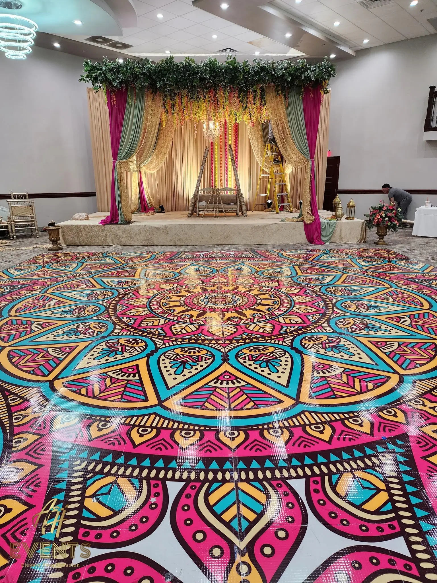 Mandala floor before a gold-draped stage with florals and a chandelier