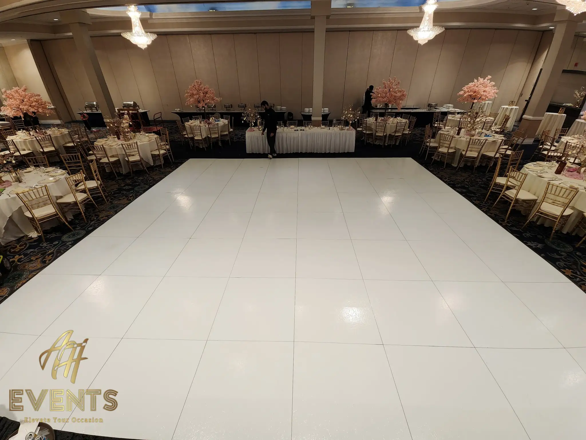 White dance floor in a ballroom with crystal chandeliers and pink blossom trees, a head table set under a painted-sky ceiling
