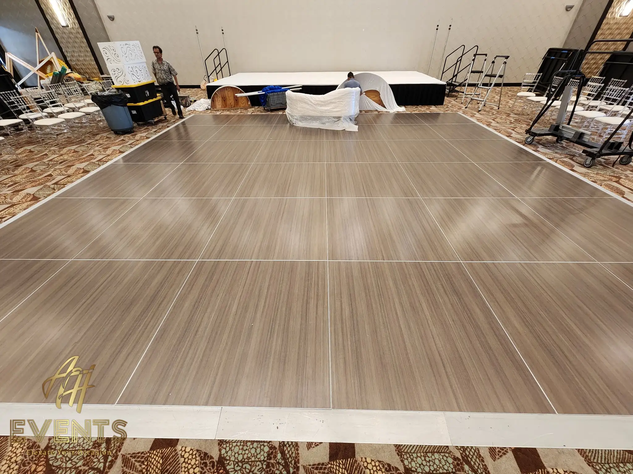 Gray wood-look dance floor being installed in a patterned-carpet ballroom during setup
