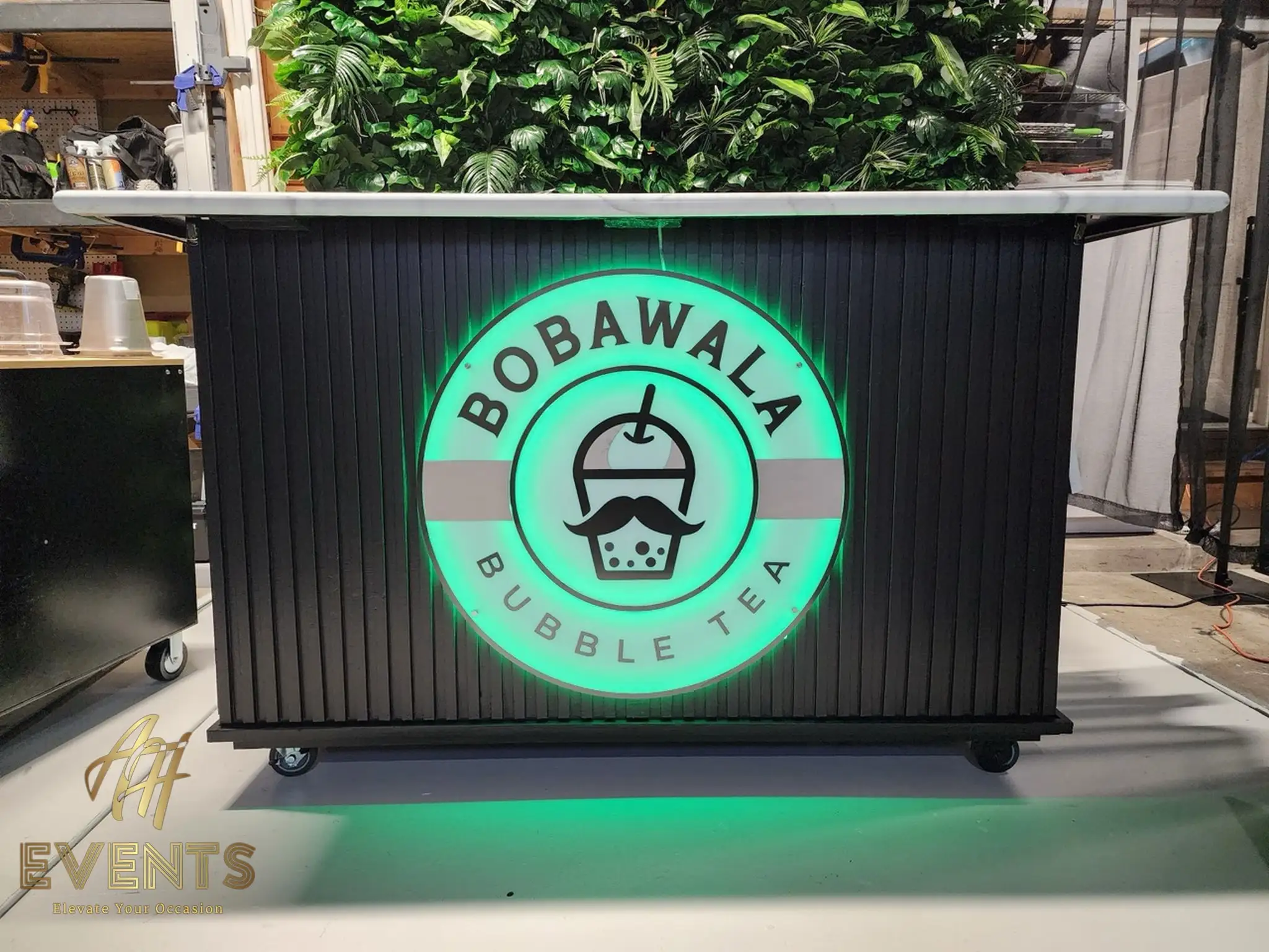 Bobawala cart on casters with its logo glowing green, set before a greenery wall in the workshop