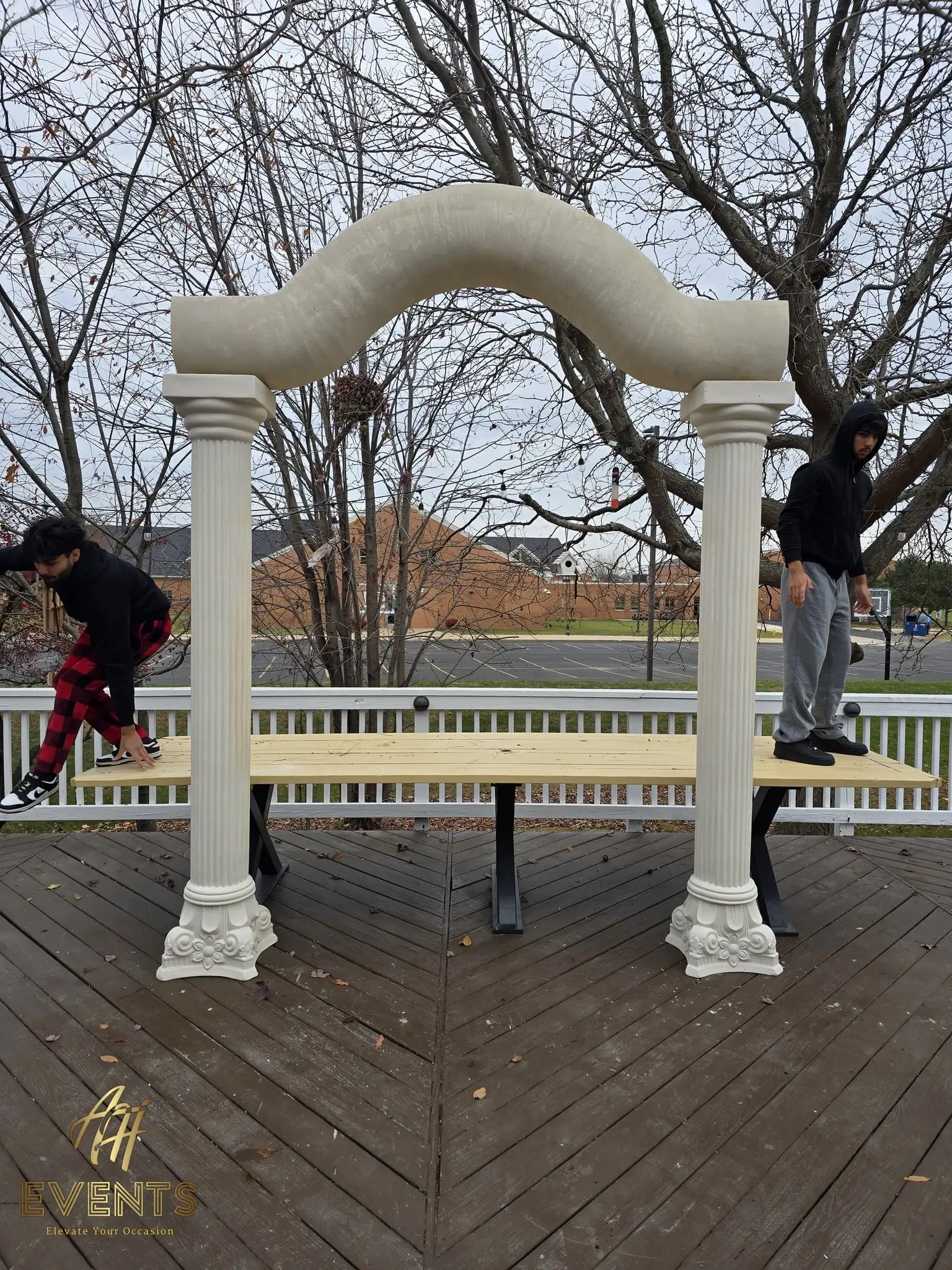 Two people assembling the fluted columns and serpentine arch over the plywood stage deck during setup