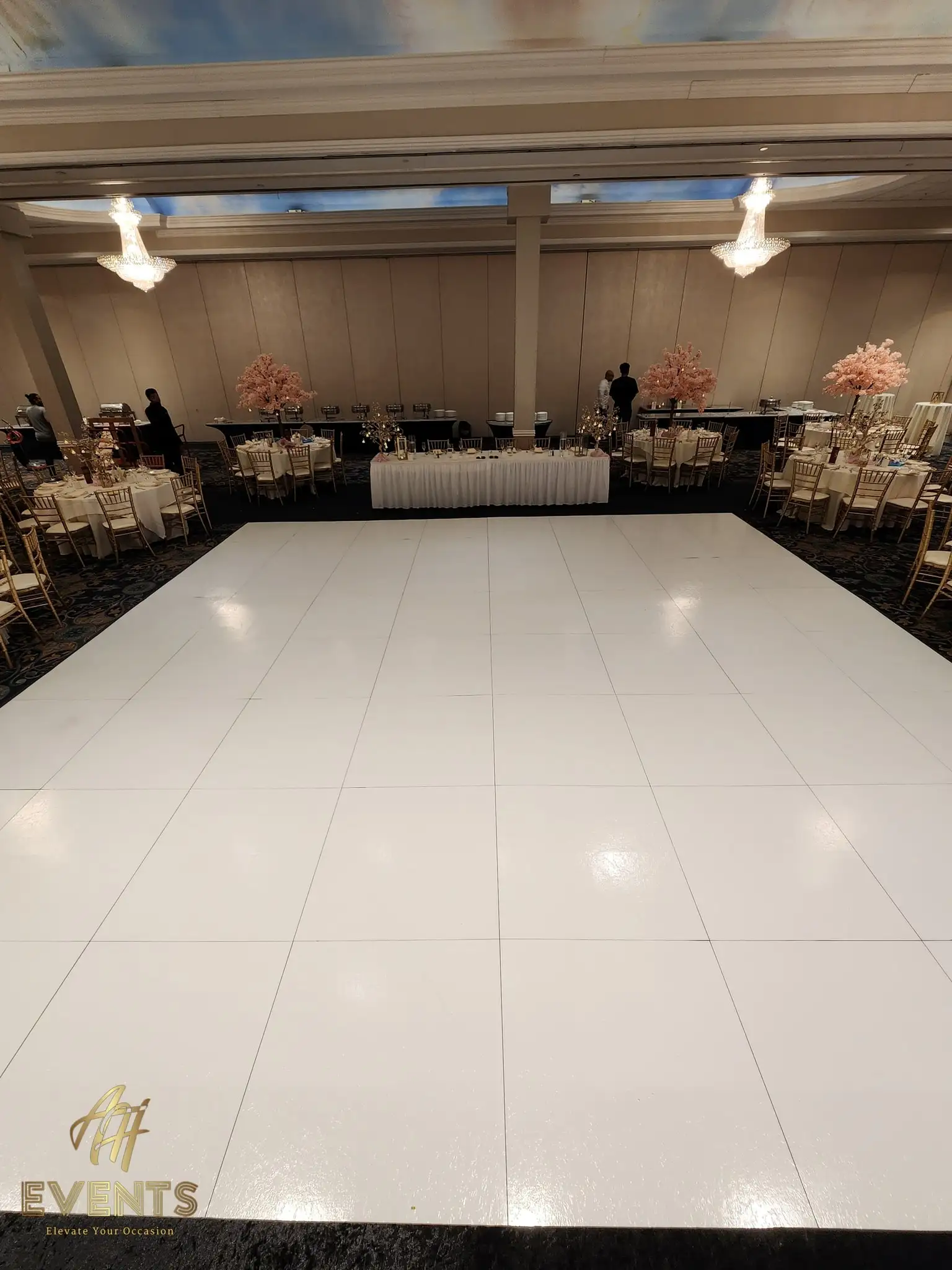 White dance floor beneath a painted-sky ceiling, flanked by pink blossom trees and a long head table