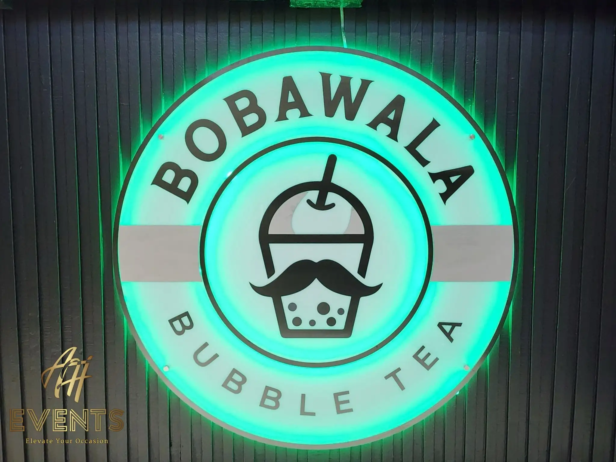 Close-up of the green-illuminated Bobawala Bubble Tea logo — a mustachioed boba cup roundel — on the cart front