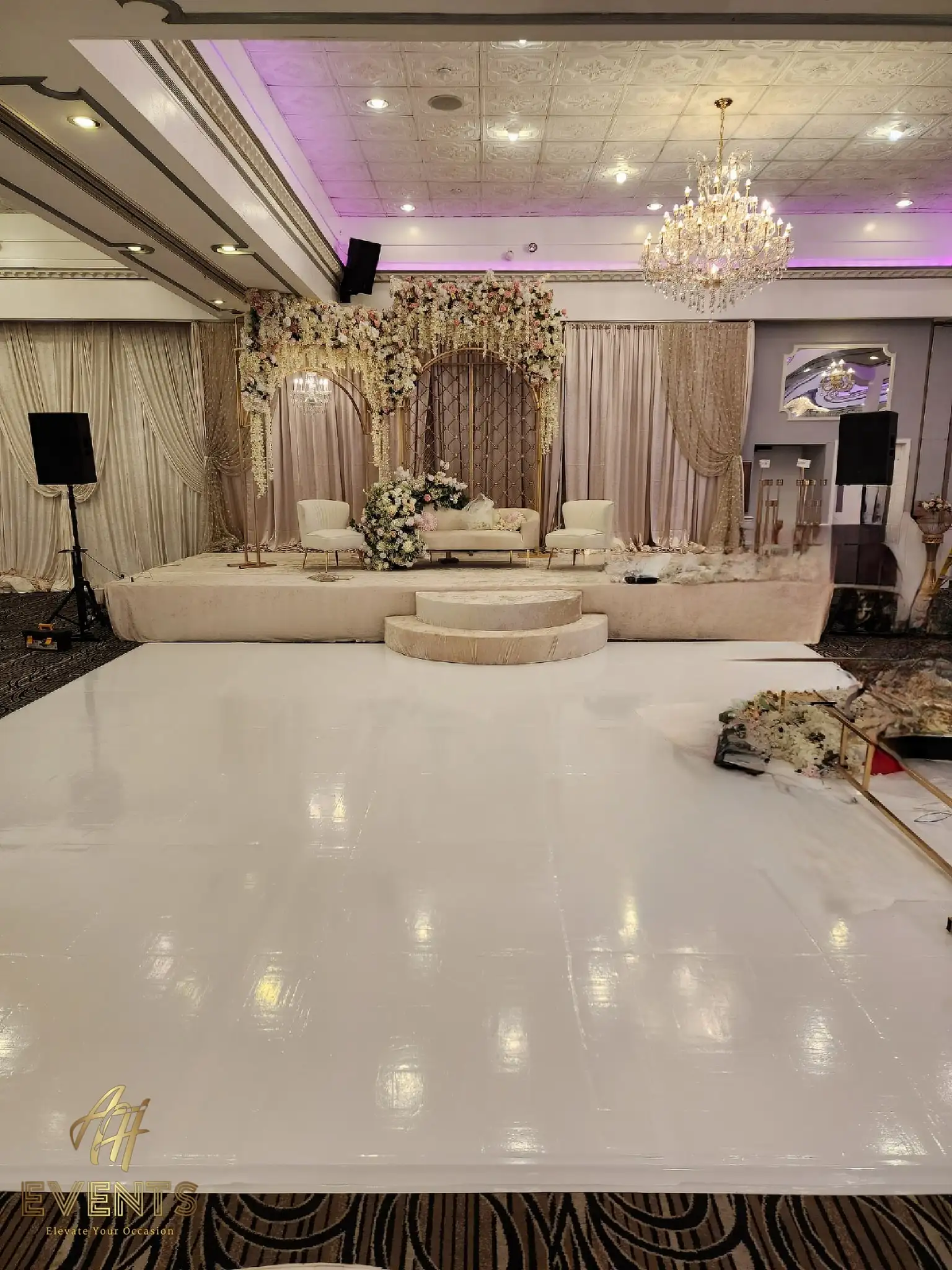 Glossy white dance floor by a blush-and-gold stage with a velvet riser and white florals
