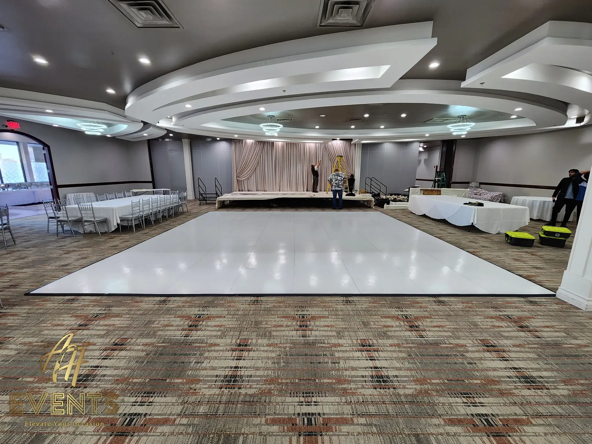 White dance floor and a low taupe-draped stage in a ballroom during setup