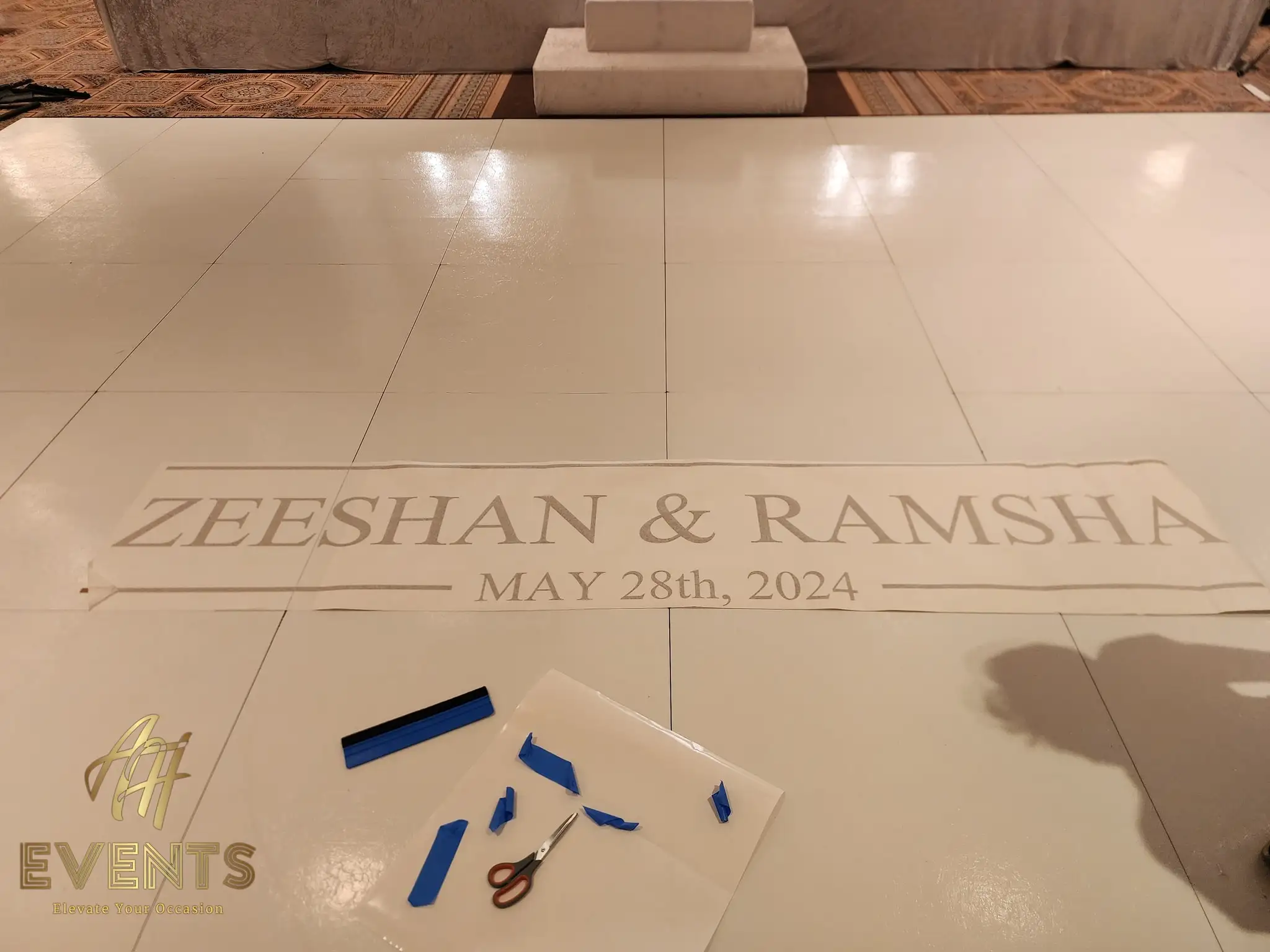 White floor printed with a 'Zeeshan & Ramsha, May 28th 2024' monogram decal, with installation tools beside it