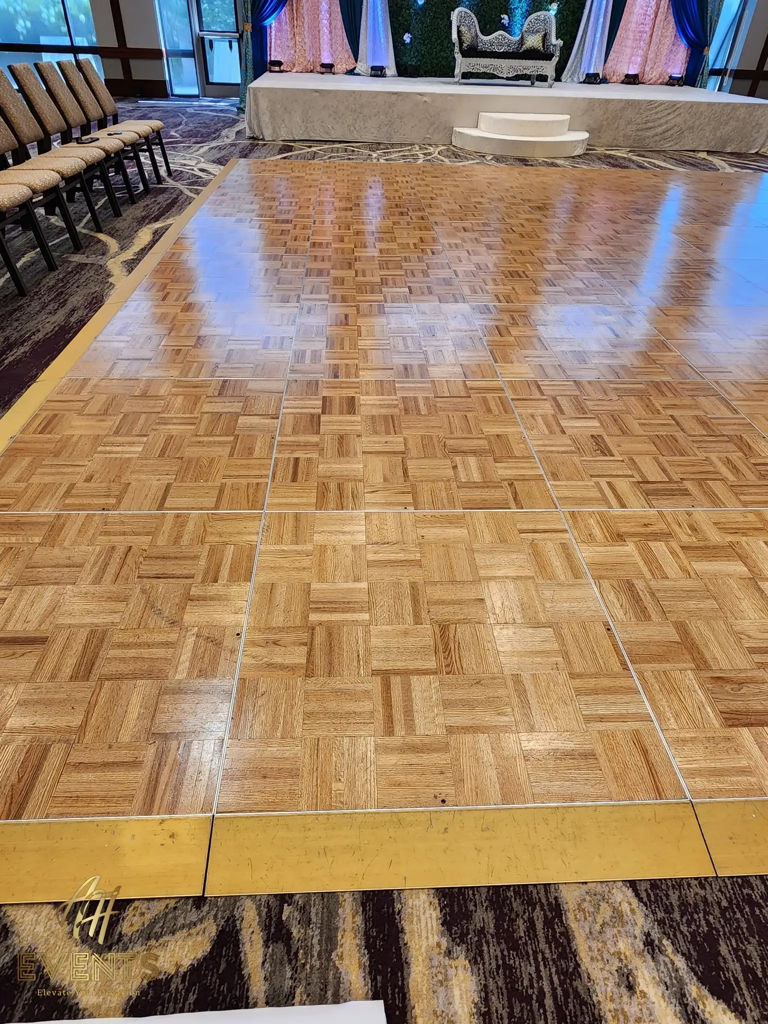 Parquet wood dance floor facing a mauve stage with a gold sofa seen through windows