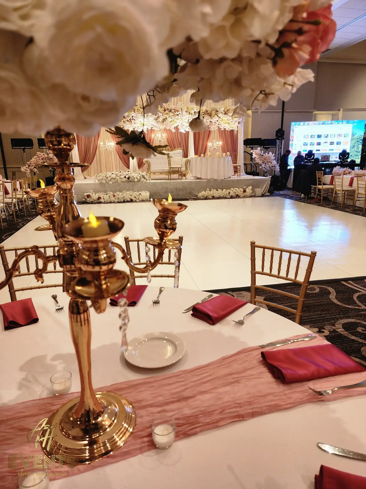 Reception table with a gold candelabra and blush runner, the white floor and blush floral stage beyond