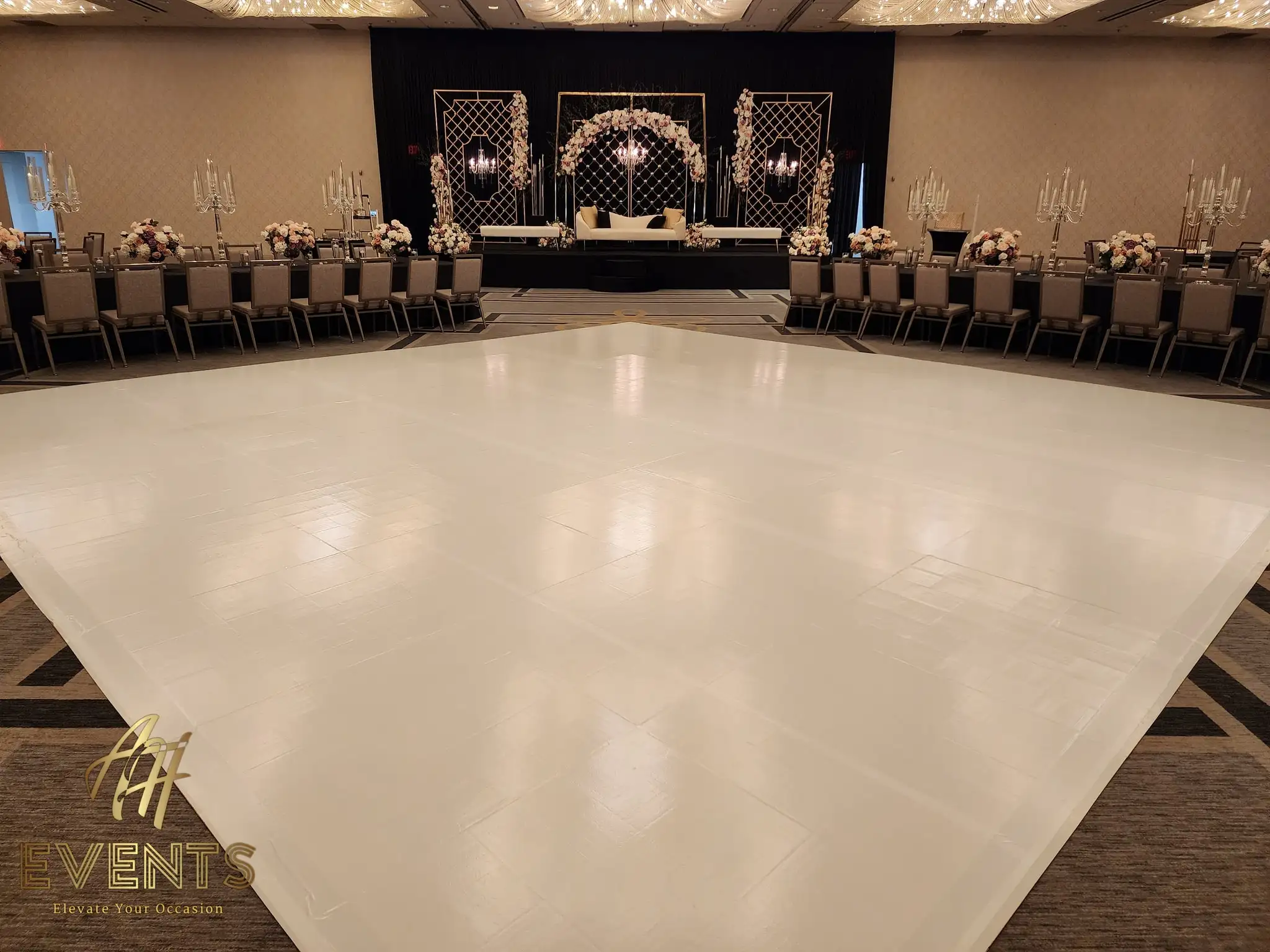Glossy white dance floor before a black stage with a floral mandap under crystal-strand lighting