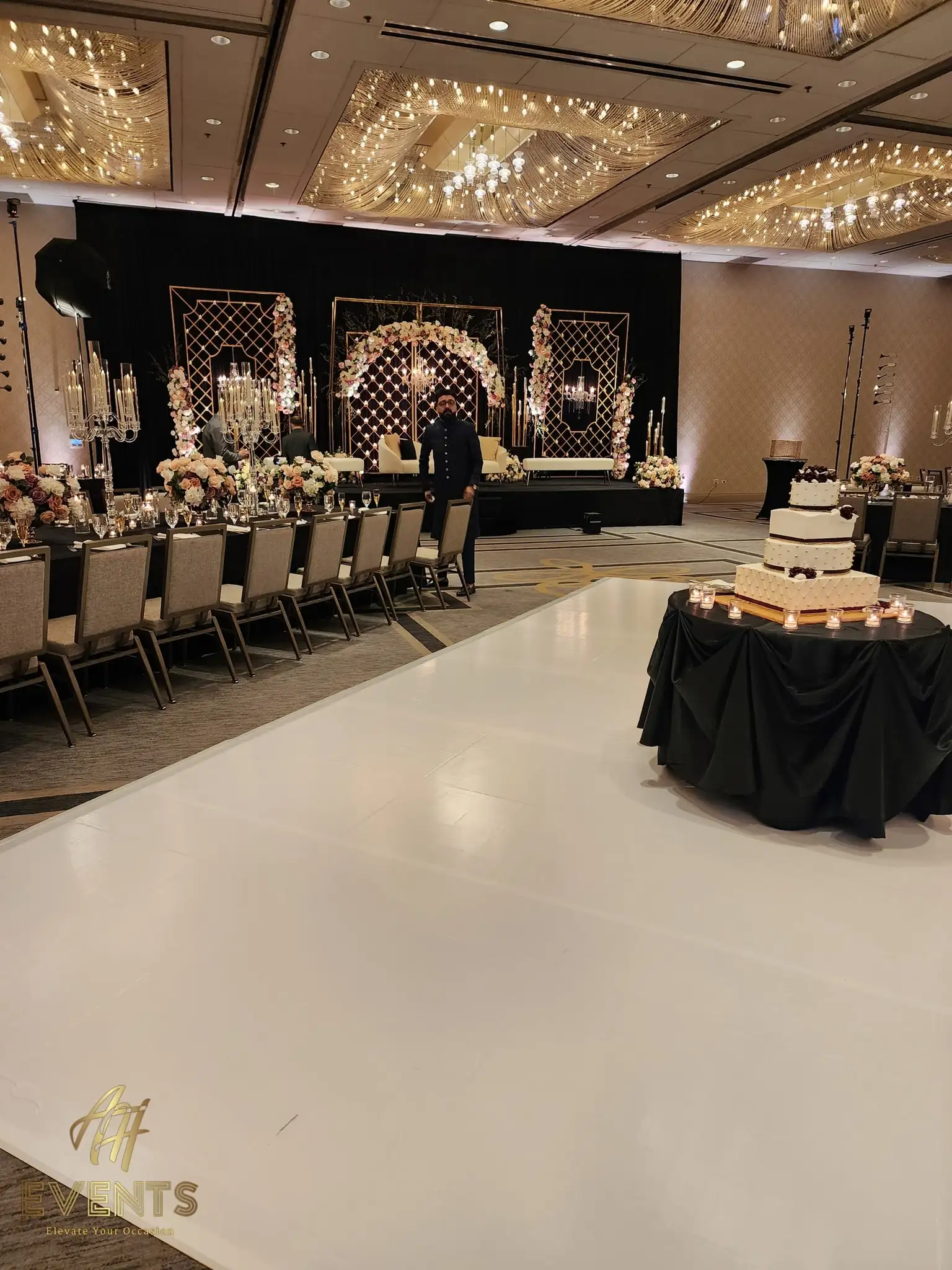 Glossy white dance floor with a black cake table, facing a black floral-mandap stage