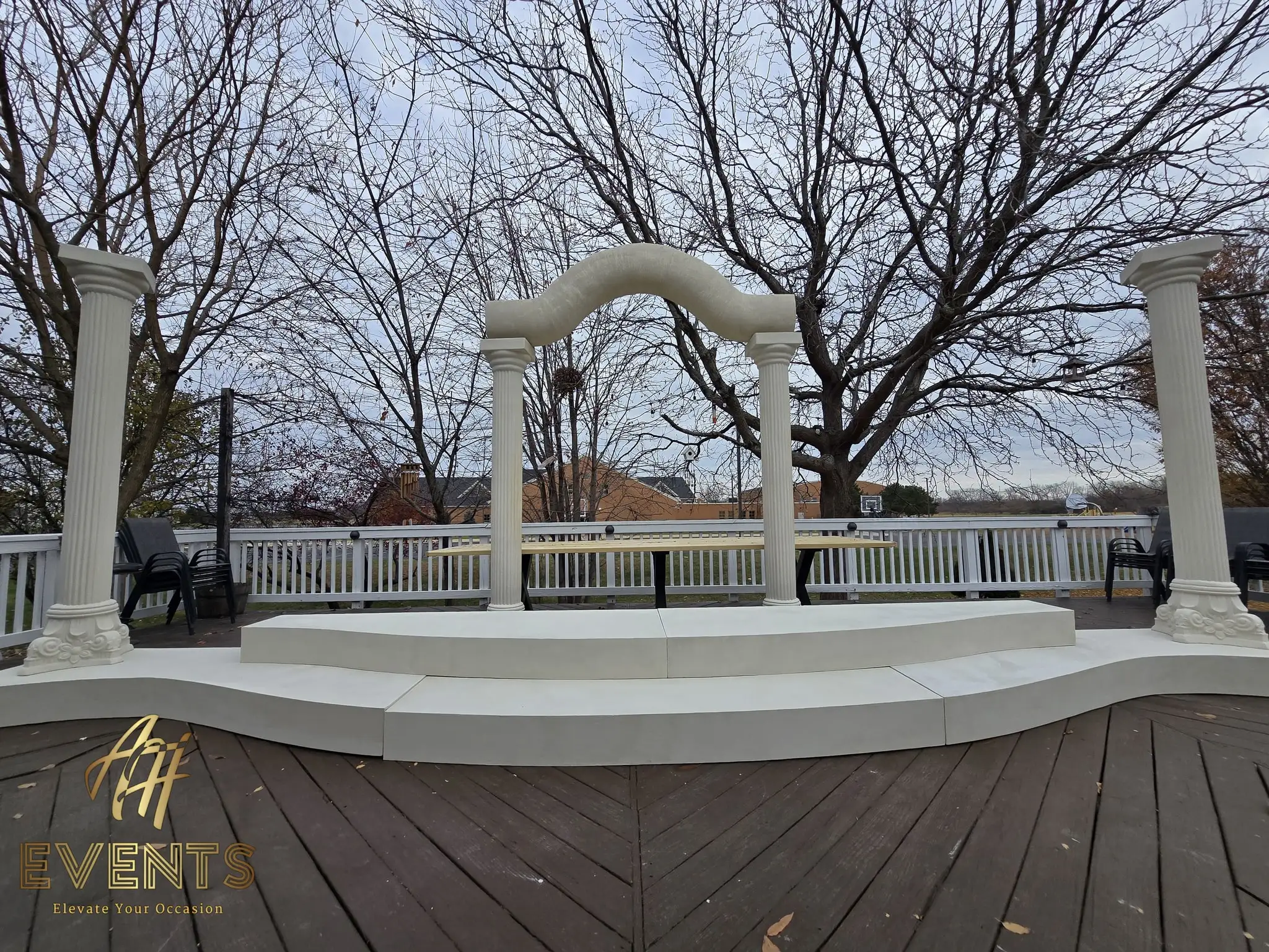 Wide view of the finished classical-pillar wedding stage — columns, serpentine arch and a curved white step base on the deck