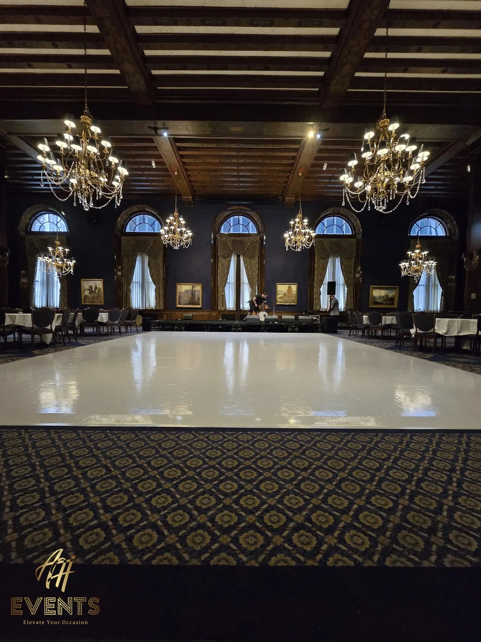 Glossy white dance floor in the wood-beamed ballroom, chandeliers and arched draped windows around