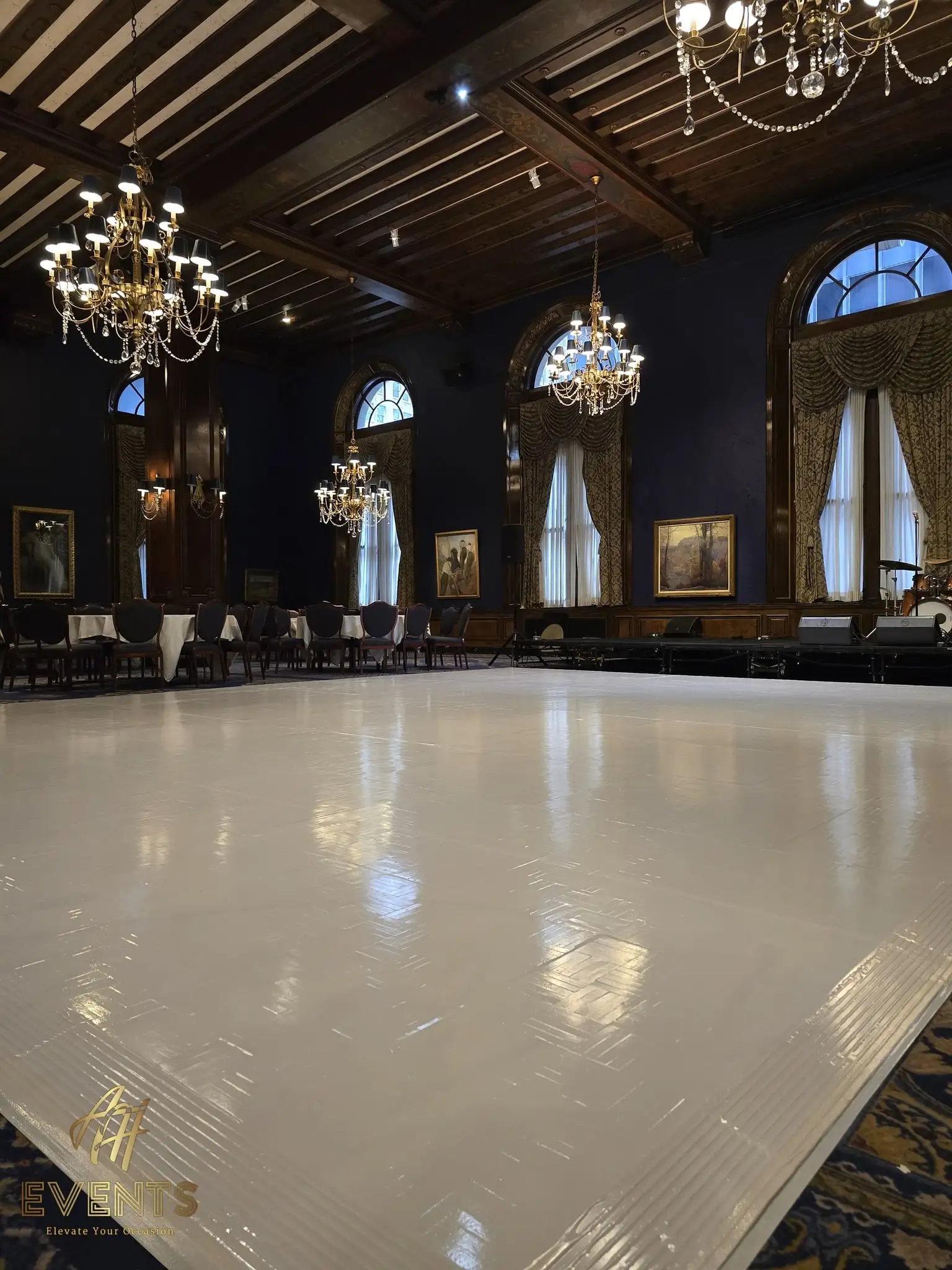 Low view of the glossy white dance floor reflecting chandeliers in the historic wood-beamed ballroom